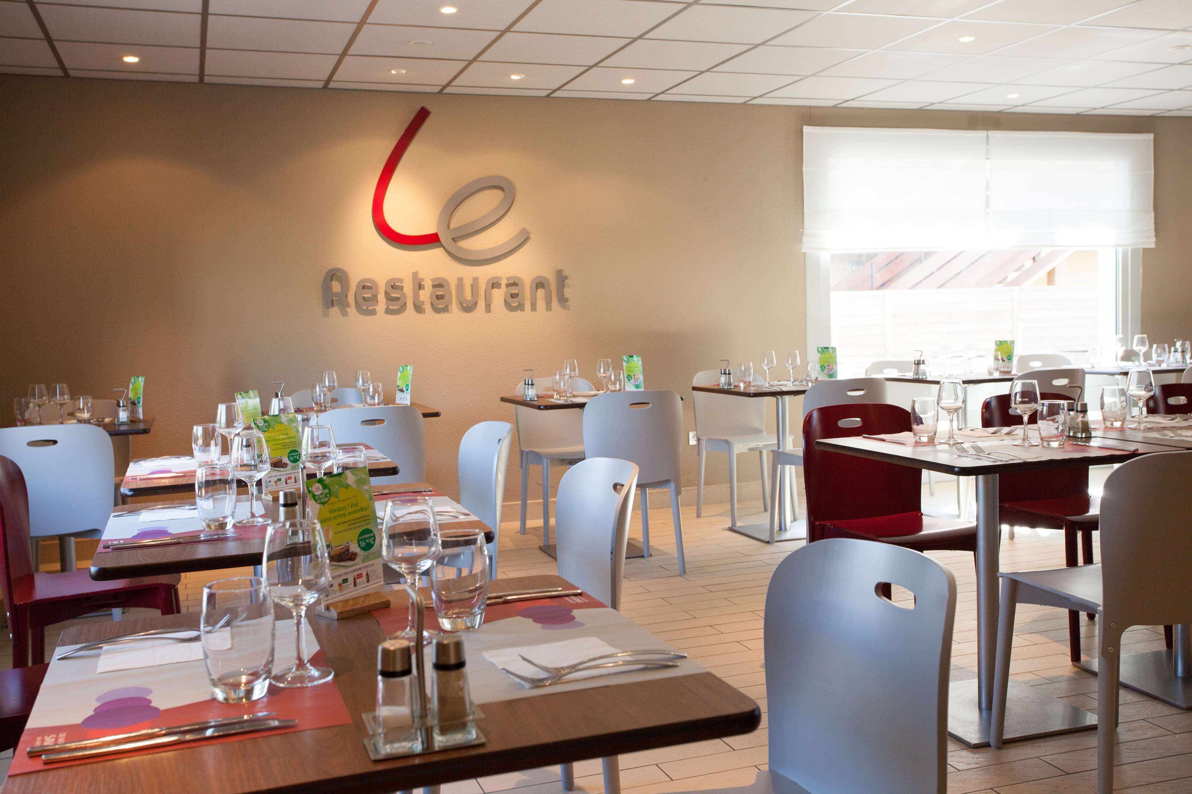 A restaurant interior with tables set for dining, chairs, and a wall sign reading "le Restaurant".