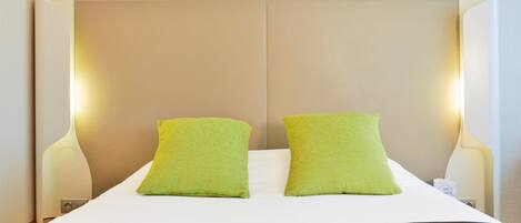 A hotel room with a bed, two green pillows, and bedside lamps.