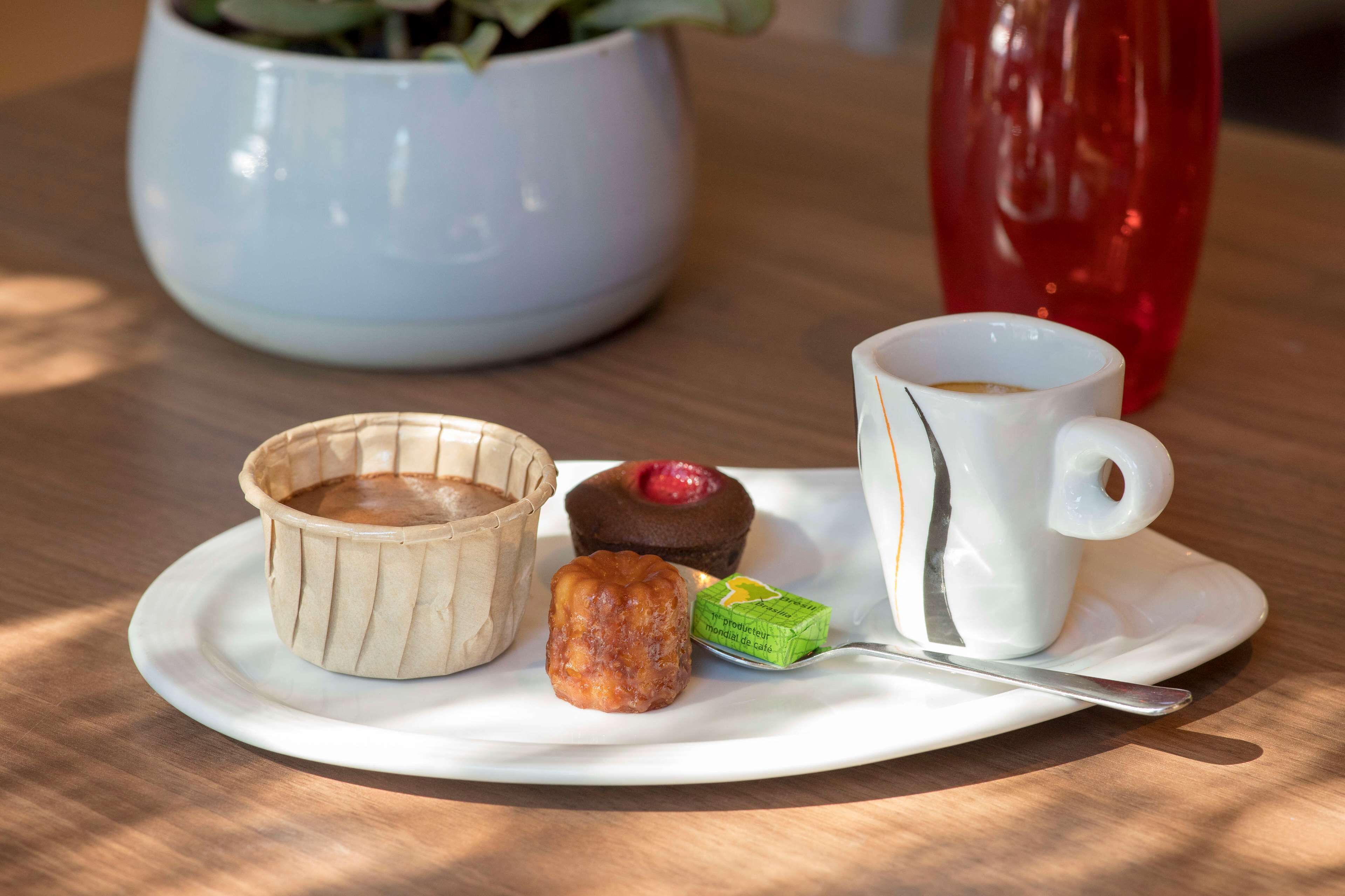 A plate with a pastry, a muffin, a small tart, a cup of coffee, and a spoon on a wooden table.