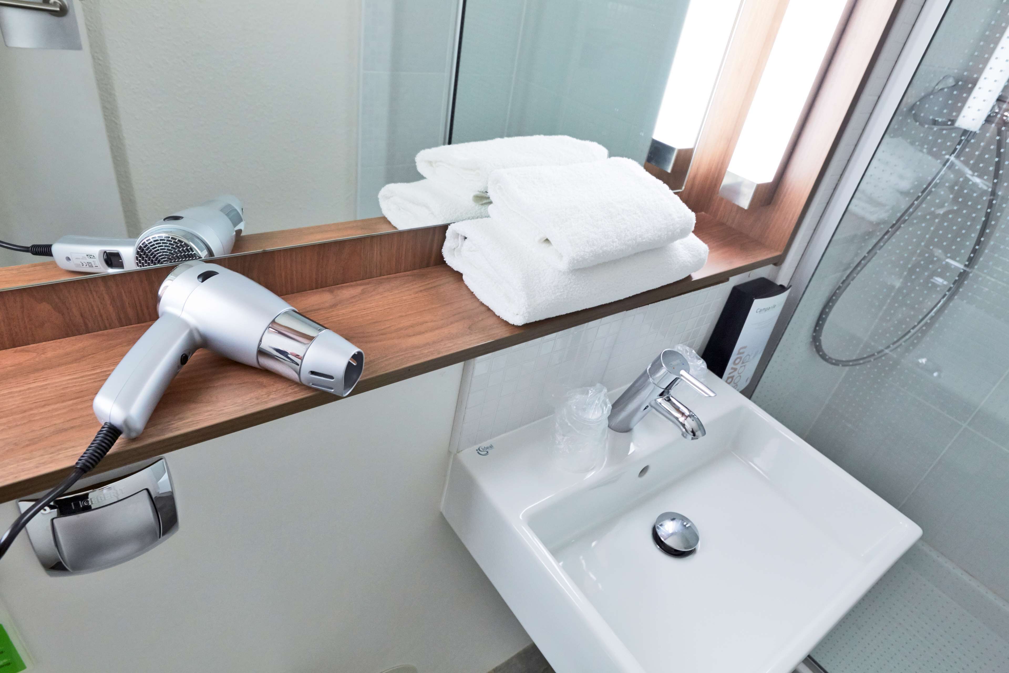 Un baño con secador de pelo sobre una repisa de madera, un lavabo con grifo y una cabina de ducha con paredes de vidrio.