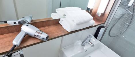Un baño con secador de pelo sobre una repisa de madera, un lavabo con grifo y una cabina de ducha con paredes de vidrio.