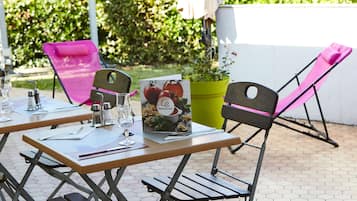 A table set outdoors with a menu, glasses, and a pink chair.