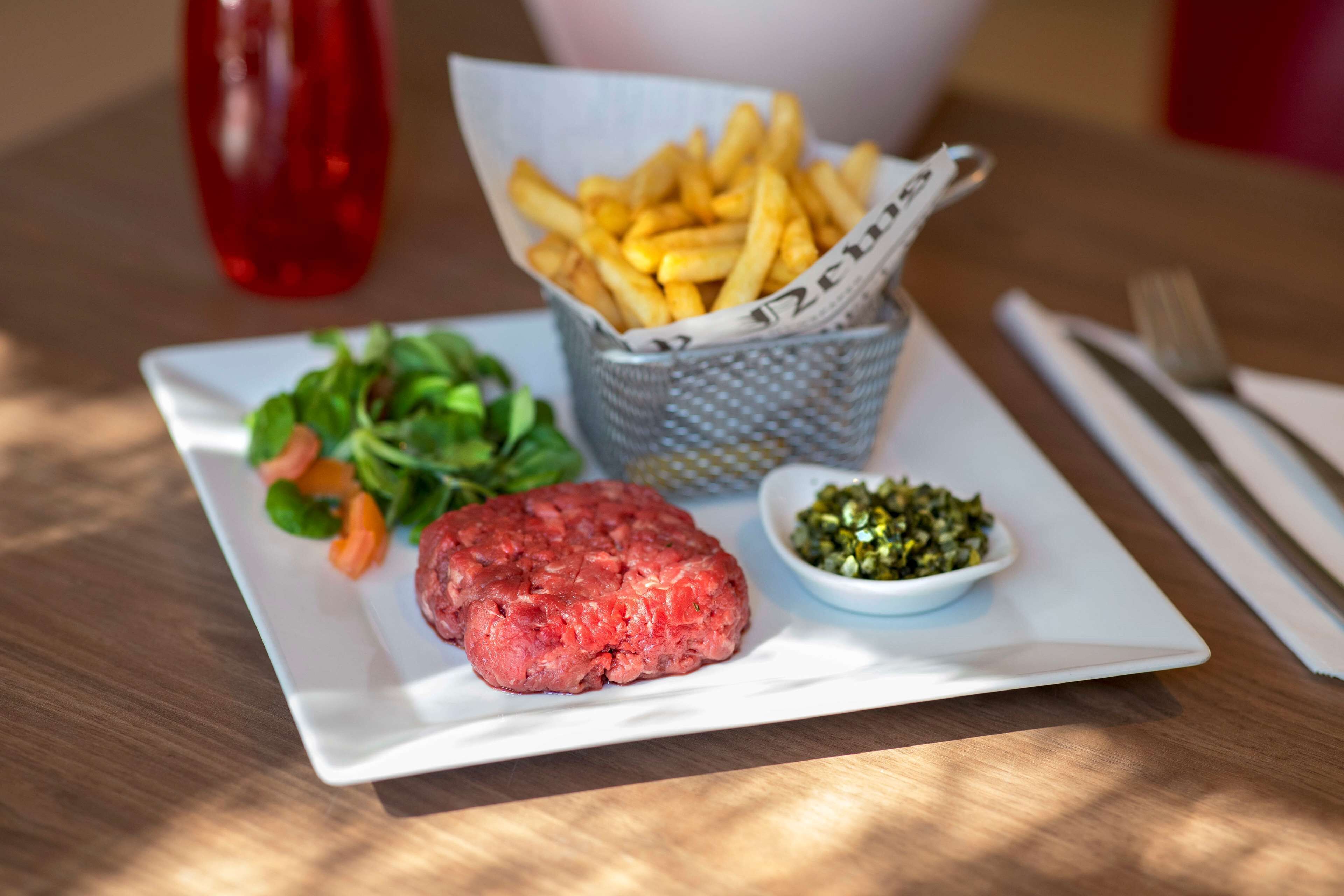 Ein Teller mit einem rohen Rinderhamburger, Pommes Frites, einem kleinen Salat und einer Schüssel grüner Soße.