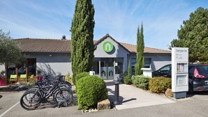 A building with a green logo, a parking area with bicycles, and a signboard. - Campanile Lyon Sud - Feyzin (Feyzin)