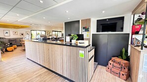 A reception desk with a wooden finish, a flat-screen TV above it, and a potted plant on the counter. - Campanile L'Isle d'Abeau - Bourgoin Jallieu (L'Isle-d'Abeau)