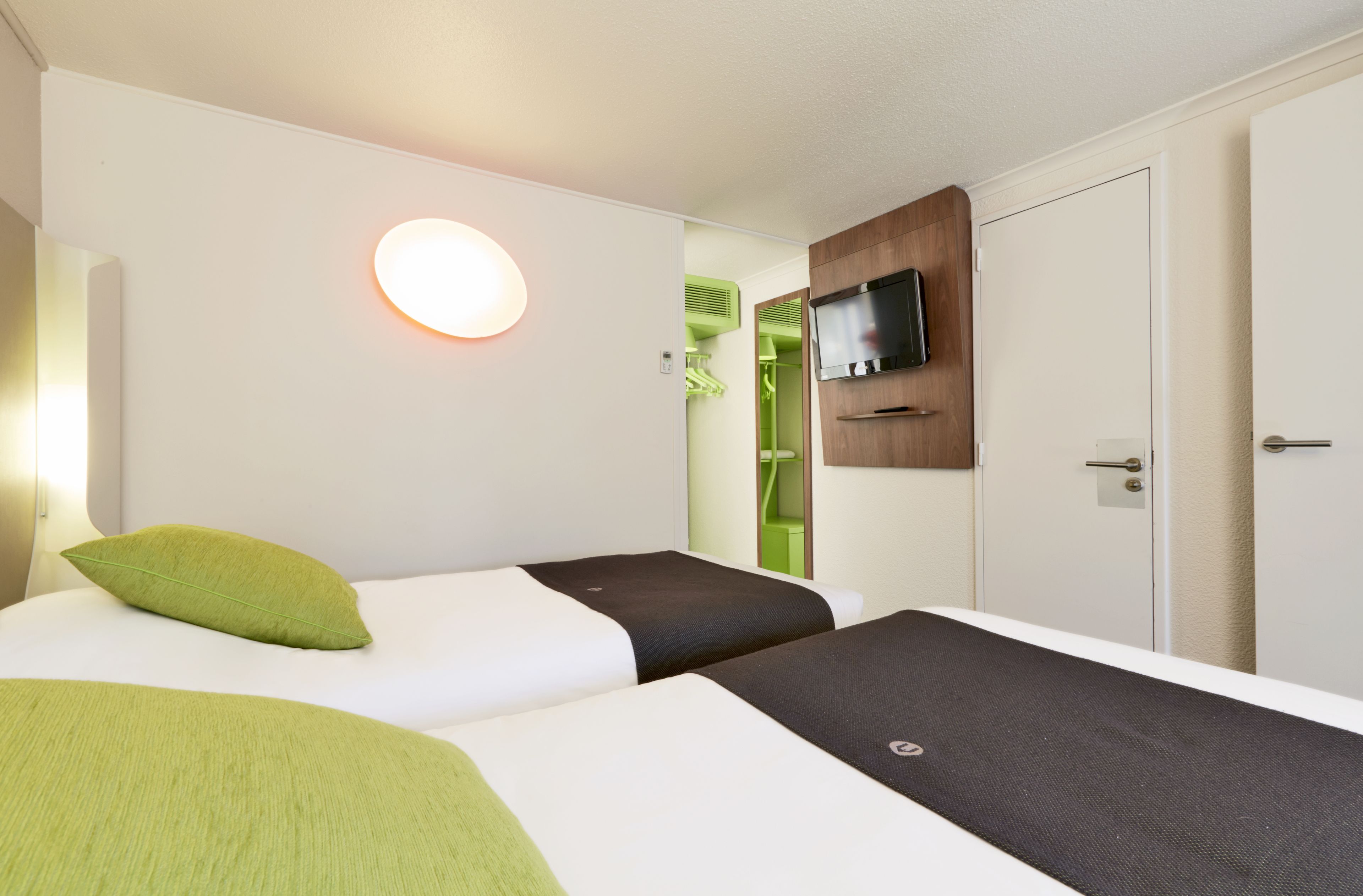 A hotel room with two beds, a TV mounted on the wall, and a door leading to a bathroom.