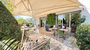 An outdoor patio area with tables and chairs, a large umbrella, and a wall with greenery. - Campanile L'Isle d'Abeau - Bourgoin Jallieu (L'Isle-d'Abeau)