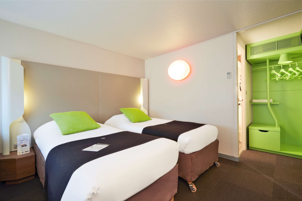 Una habitación de hotel con dos camas, un armario verde y una mesita de noche con lámpara.