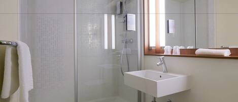 A modern bathroom with a glass-enclosed shower, a white sink, and a mirror above it.