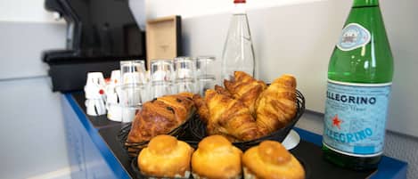 A breakfast buffet with croissants, muffins, and a bottle of Pellegrino water.