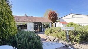 A hotel entrance with a sign indicating a reception area, a tiled roof, and a small garden with shrubs. - Campanile L'Isle d'Abeau - Bourgoin Jallieu (L'Isle-d'Abeau)