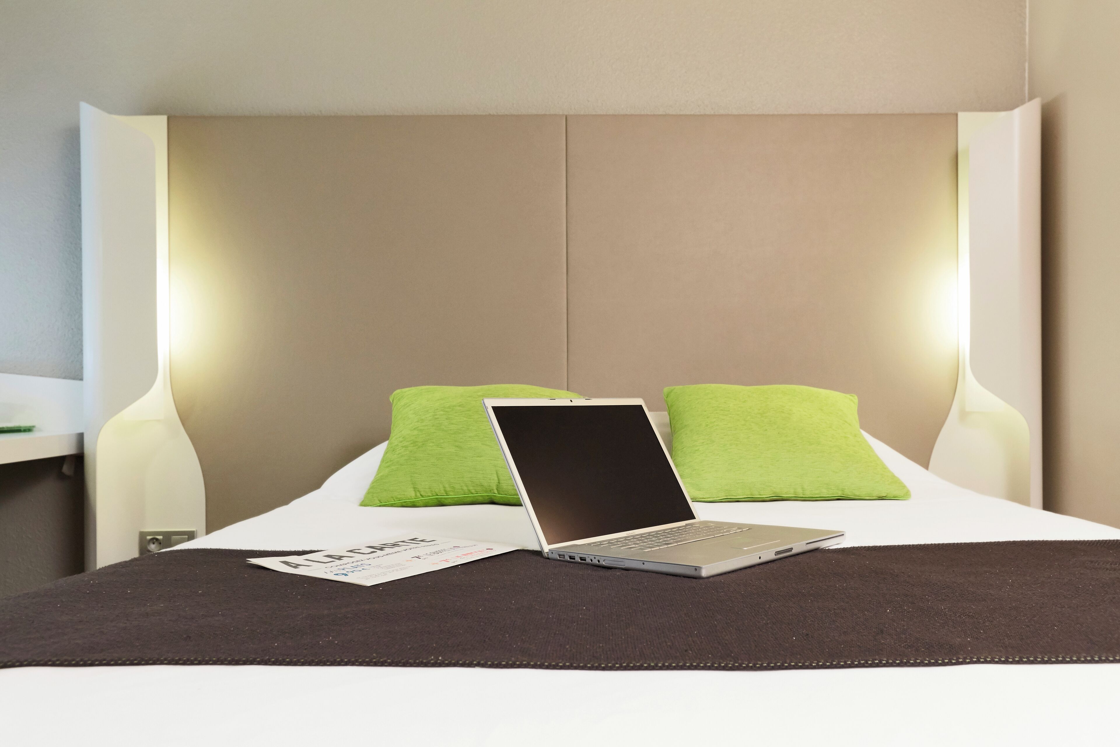 A neatly made bed with a laptop on it, two green pillows, and a white headboard.