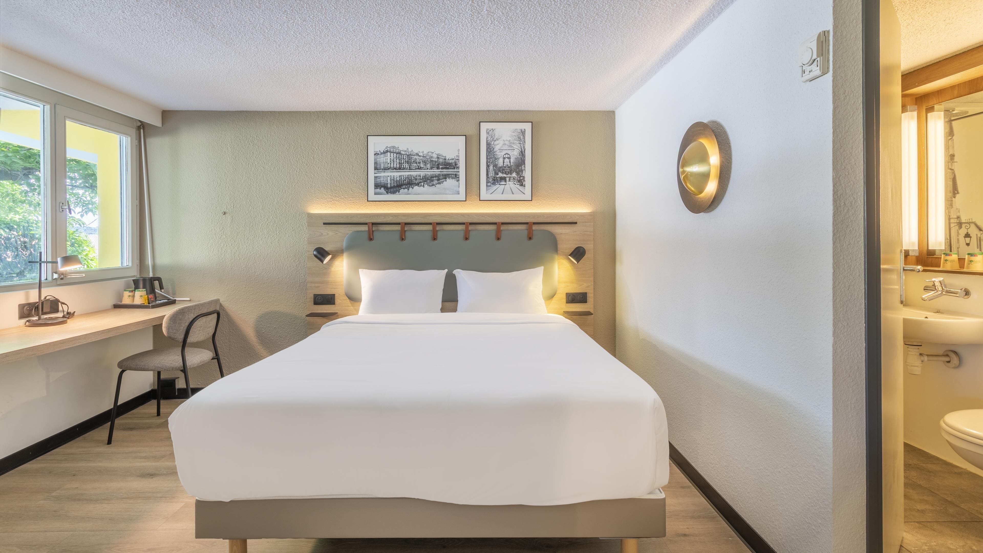 Une chambre d’hôtel comprenant un lit, un bureau, une chaise et une salle de bain avec un lavabo et un miroir.