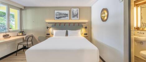 A hotel room with a bed, desk, chair, and a bathroom with a sink and mirror.