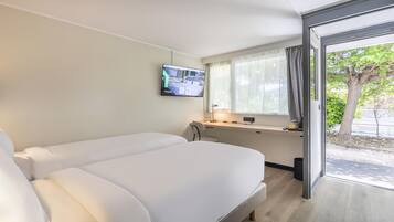 Une chambre d’hôtel avec un lit, un bureau, une télévision et une fenêtre donnant sur des arbres.
