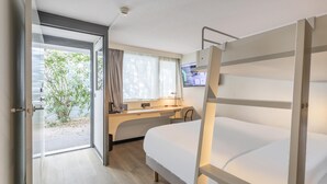 Habitación de hotel con literas, un escritorio con computadora, una ventana con cortinas y vista a zonas verdes.