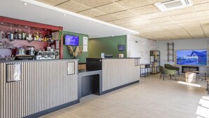 Zona de bar con una variedad de botellas de licor, una máquina de café y una pantalla de televisión mostrando 'Campanile Nature'.