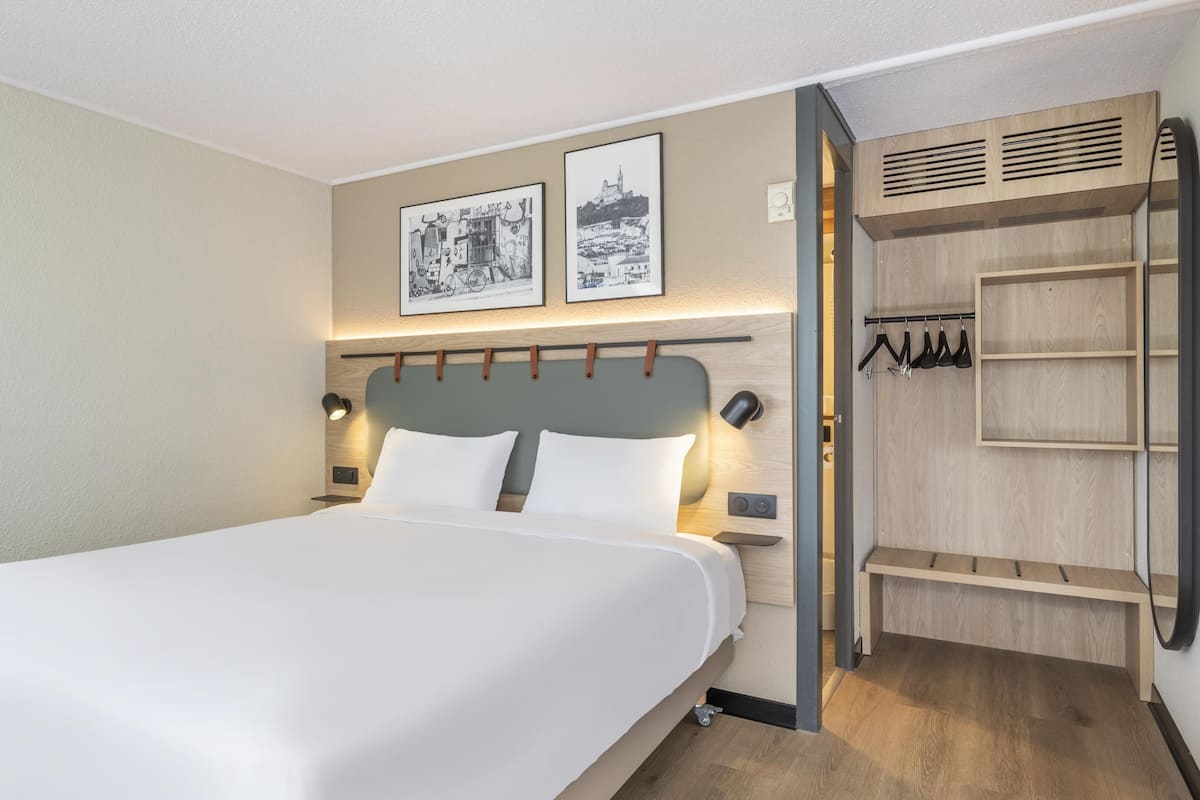 A hotel room with a bed, bedside lamps, a wardrobe, and two framed pictures on the wall.
