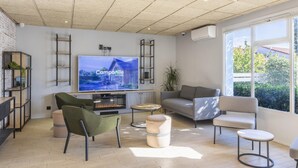 Un salón moderno con televisor de pantalla plana, asientos cómodos, chimenea y ventanas amplias que dan a vistas de vegetación.
