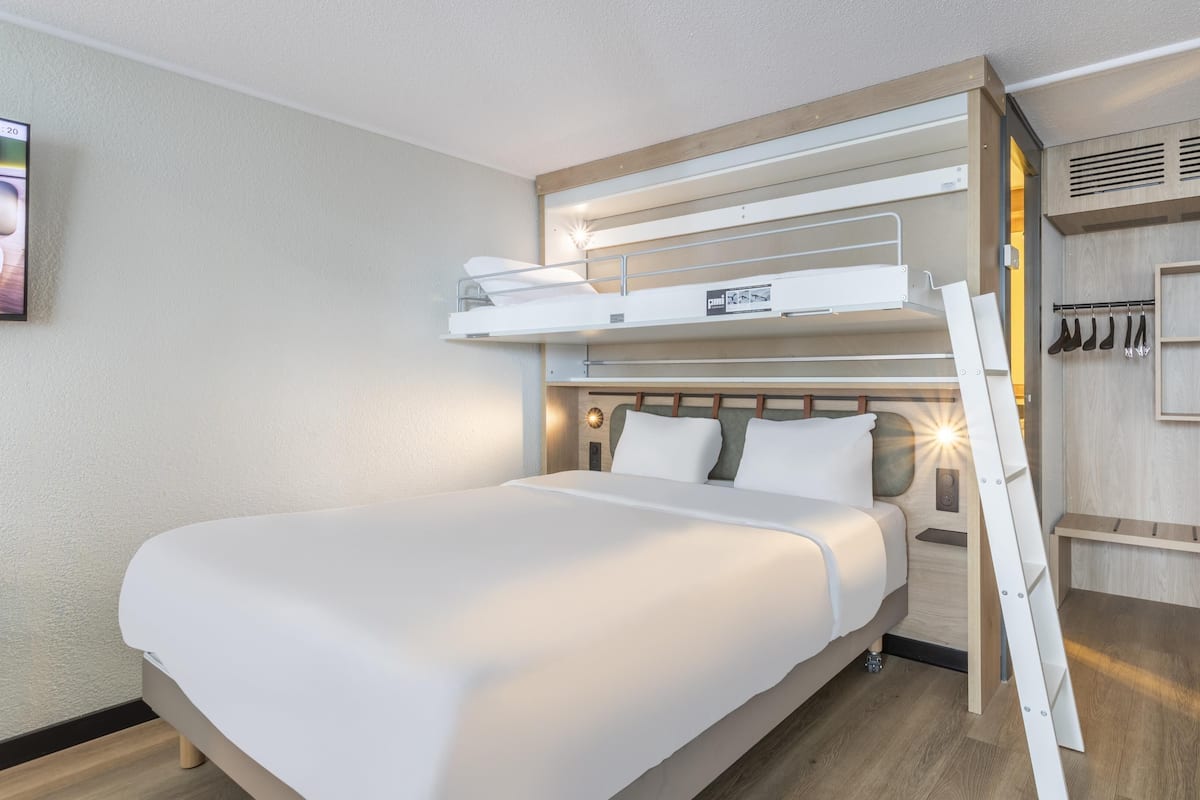 A modern hotel room with a bunk bed, a wardrobe with built-in shelves, and a bedside table.
