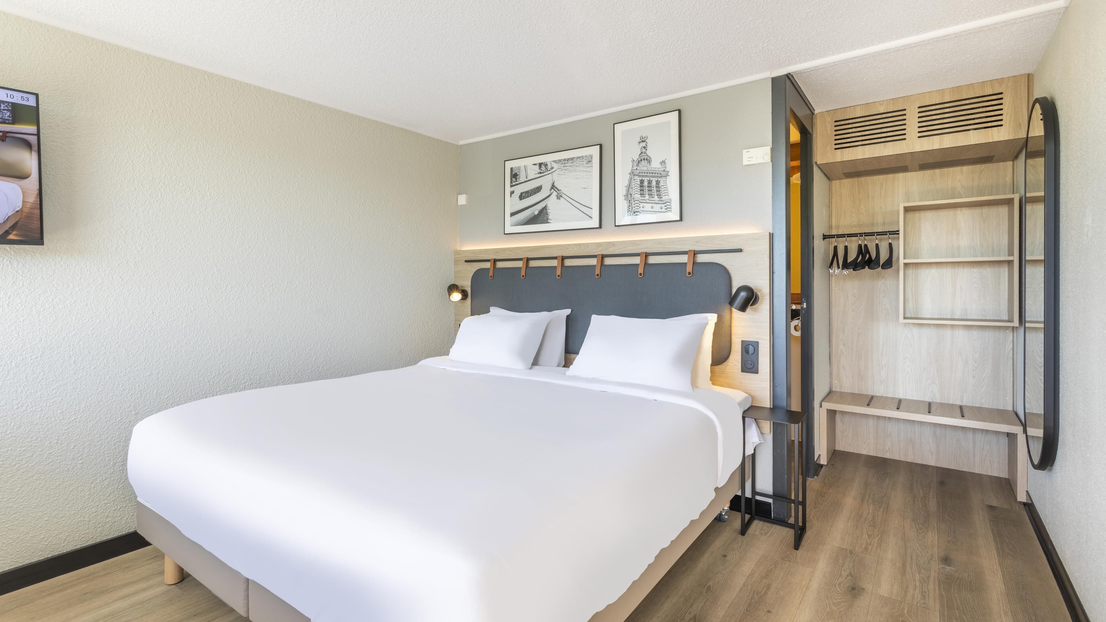 Une chambre d’hôtel moderne avec un grand lit, une armoire en bois et deux tableaux encadrés au mur.