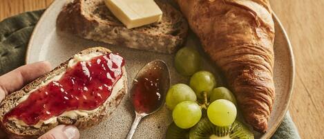 A plate with a croissant, a slice of bread with jam, grapes, kiwi slices, and a spoon.