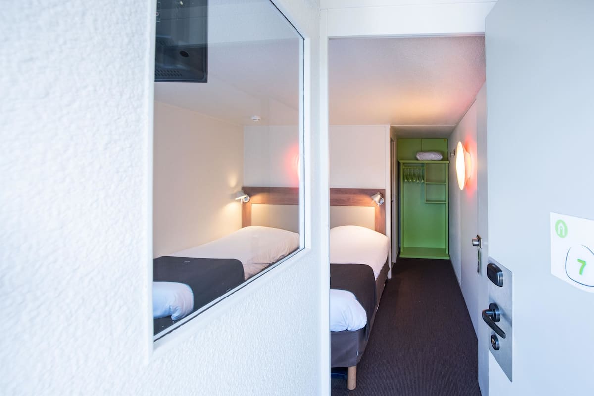 A narrow hallway with two beds, a green door, and a wall-mounted light fixture.