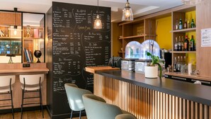Zona de bar con un men ú en pizarra que enumera bebidas y precios, taburetes y una estantería con botellas.