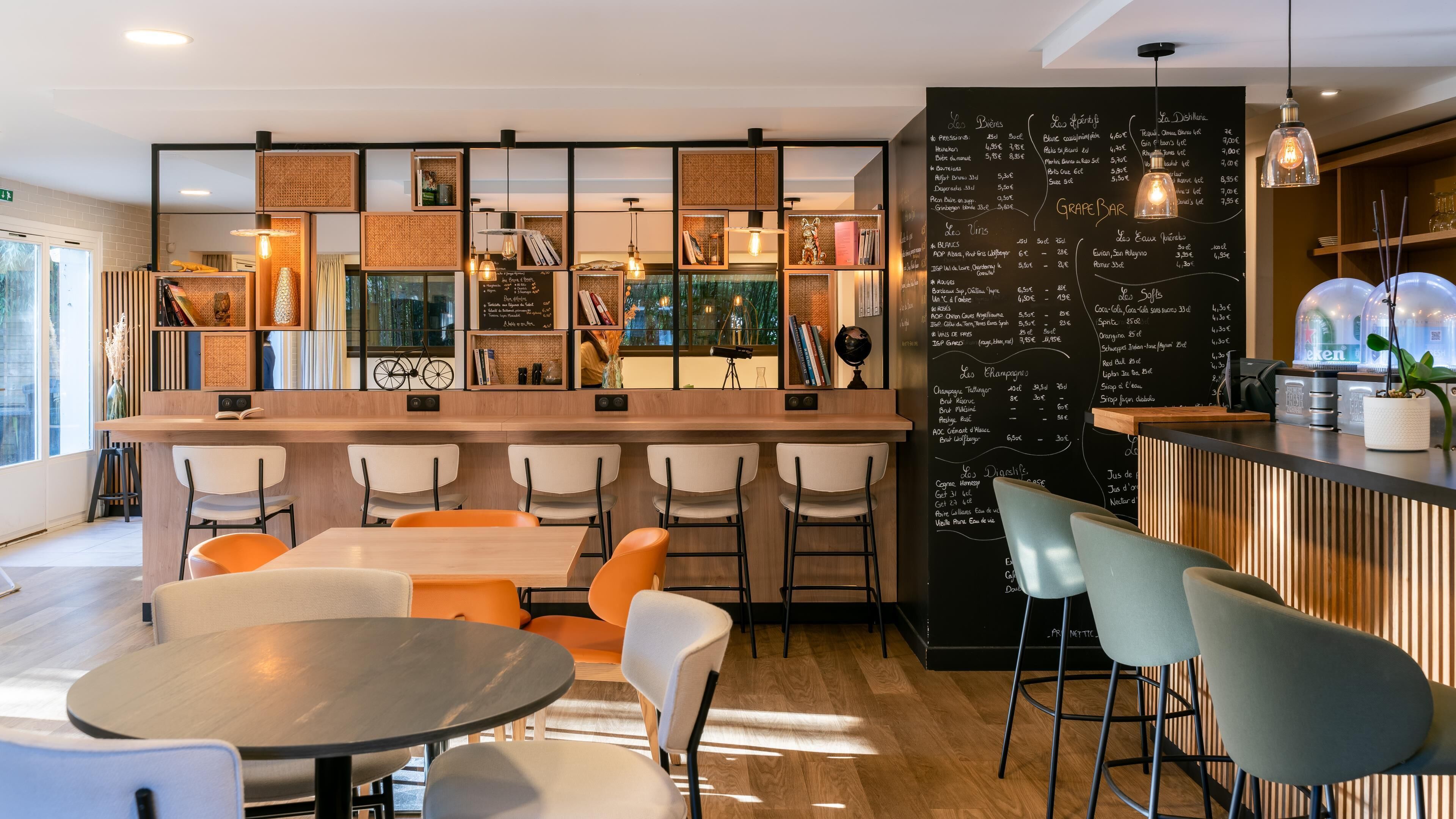 A modern bar area with a blackboard menu, white chairs, and a wooden counter.