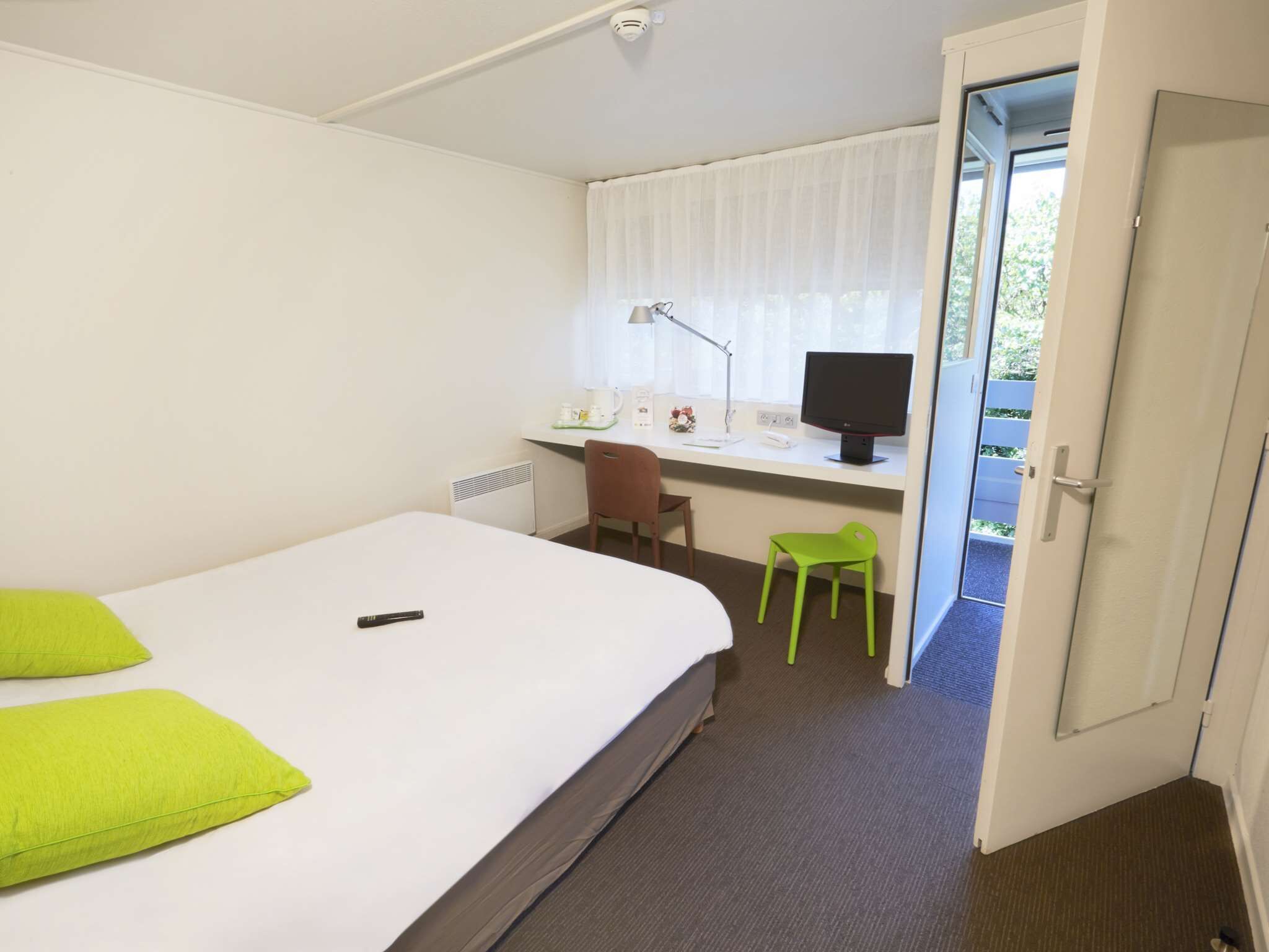 Une chambre d’hôtel avec un lit, un bureau avec un ordinateur, une chaise et une fenêtre avec des rideaux.