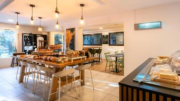 A modern cafe with a wooden counter, green chairs, and a variety of breakfast items.