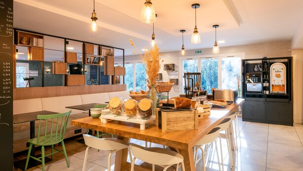 Un café moderno con una mesa de madera, sillas verdes y blancas, diversos alimentos y una máquina de café.