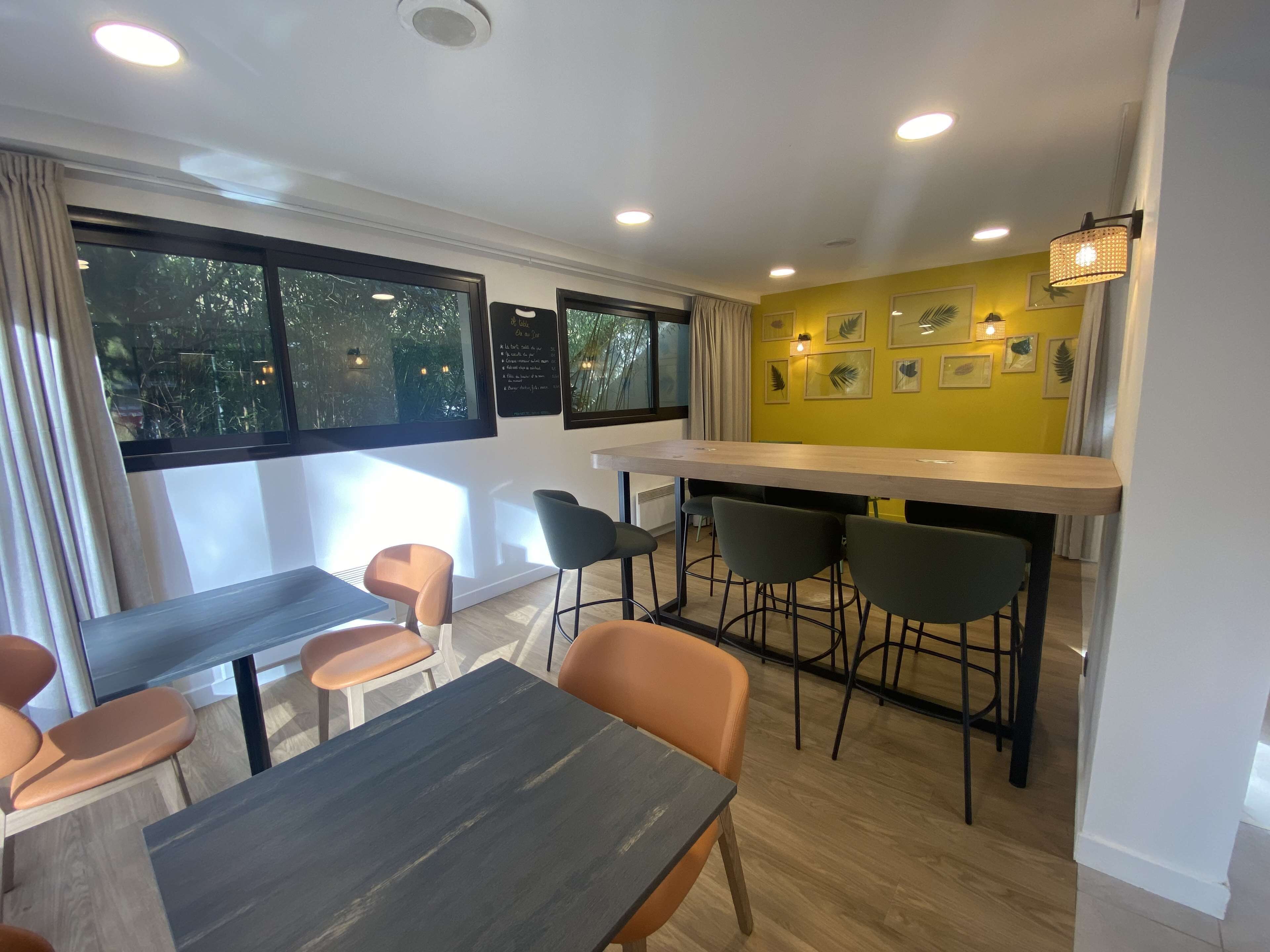 A modern dining area with a bar, multiple seating options including bar stools and chairs, and large windows providing natural light.