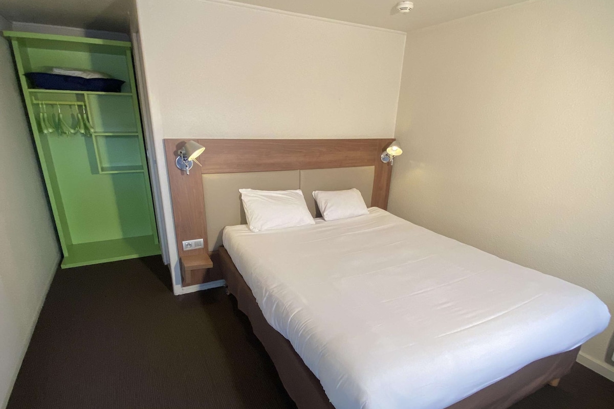 A hotel room with a bed, a green wardrobe, and a nightstand with a lamp.