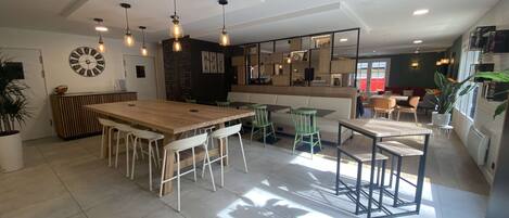 A spacious dining area with a large wooden table and multiple chairs, a wall clock, and pendant lighting.