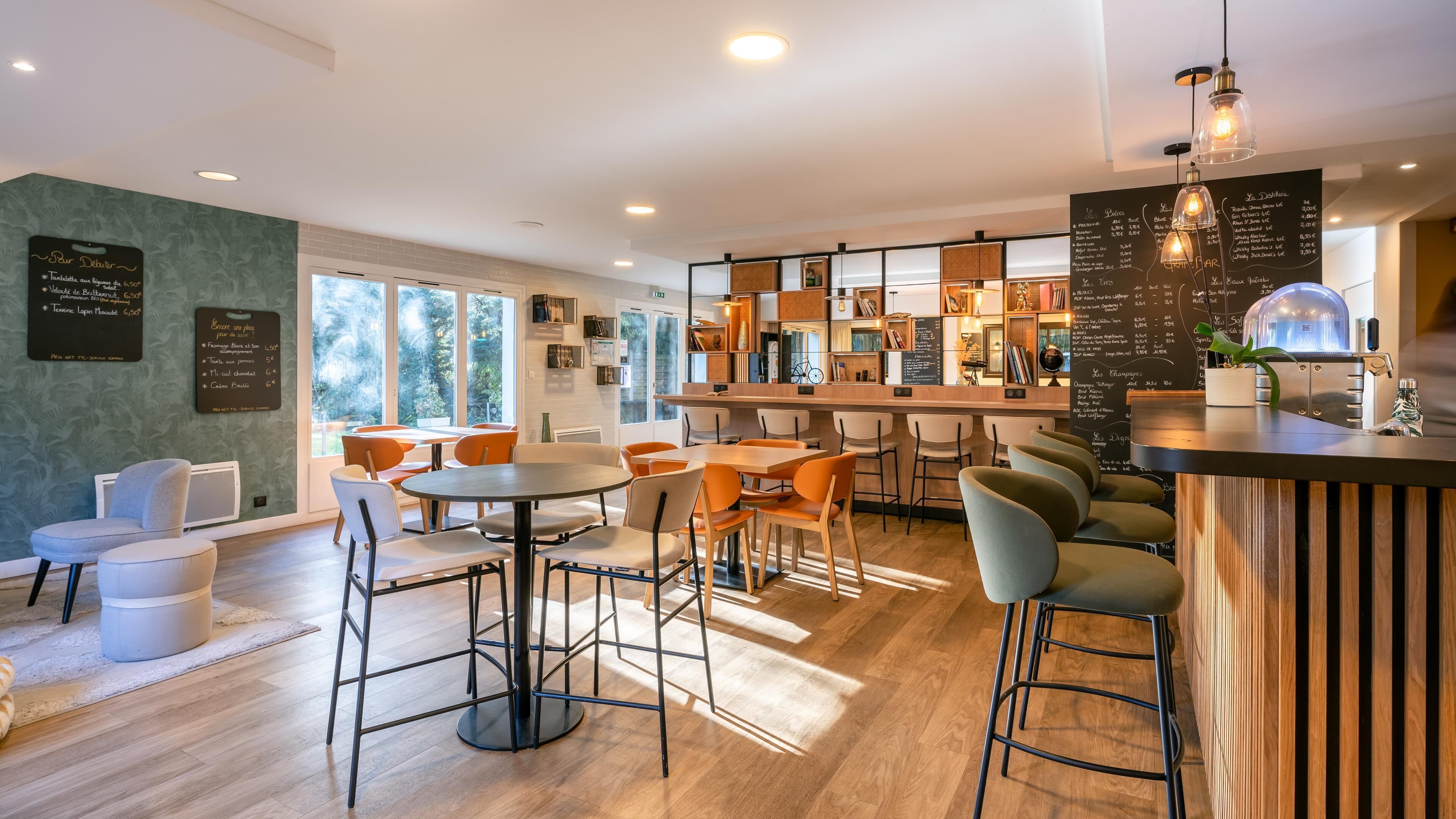 A modern restaurant with a bar area, wooden flooring, and a view of greenery outside.