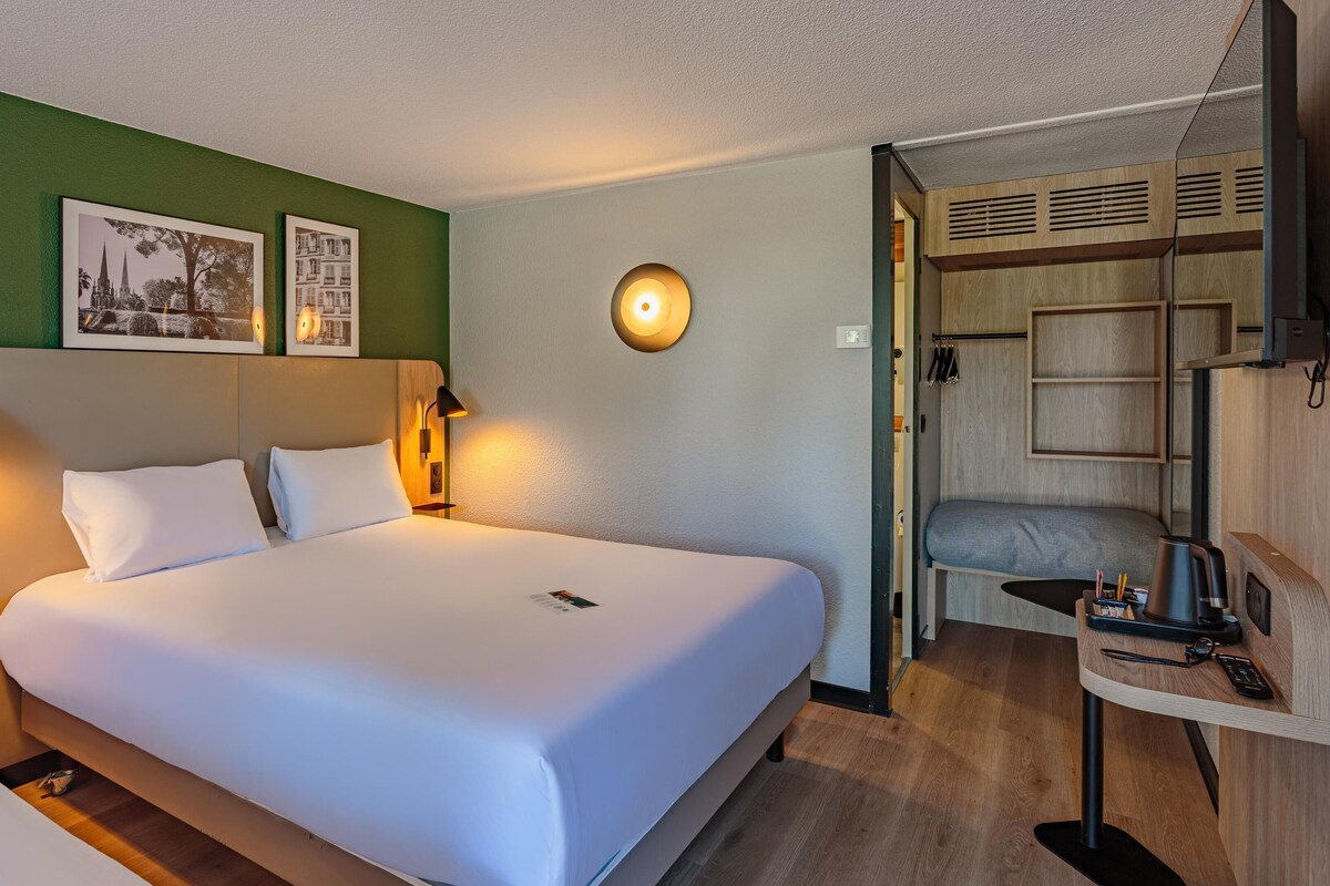 A hotel room with a large bed, two bedside lamps, a wall-mounted light, and a small table with a remote control.