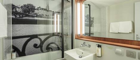 A bathroom with a glass shower enclosure, a sink, and a mirror.