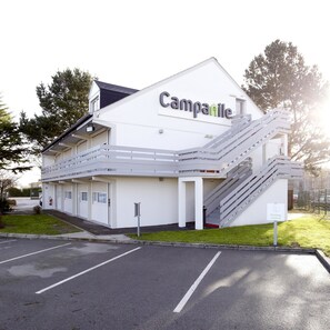 A modern building with a sign reading "Campanile." It features a staircase leading to an upper level, a parking lot in front, and a grassy area. - Hotel Campanile Nantes Ouest - Saint Herblain (Saint-Herblain)