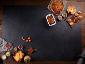 Verschiedene Desserts und Backwaren auf einer dunklen Schieferplatte, darunter ein Kuchen, Brot mit Sahne und Ananas.
