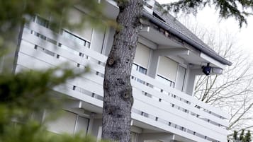 Un edificio de varios pisos con fachada blanca, balcones y un árbol en primer plano.