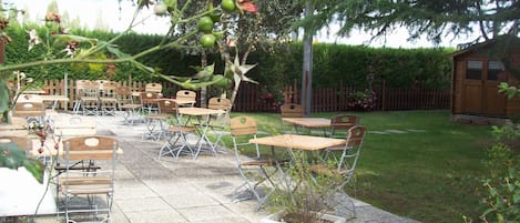An outdoor patio with tables and chairs, surrounded by a wooden fence and a garden.