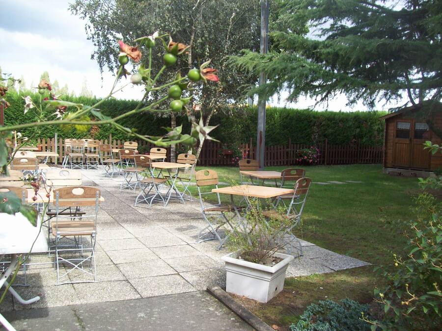 Une terrasse extérieure avec des tables et des chaises, entourée d’une clôture en bois et d’un jardin.