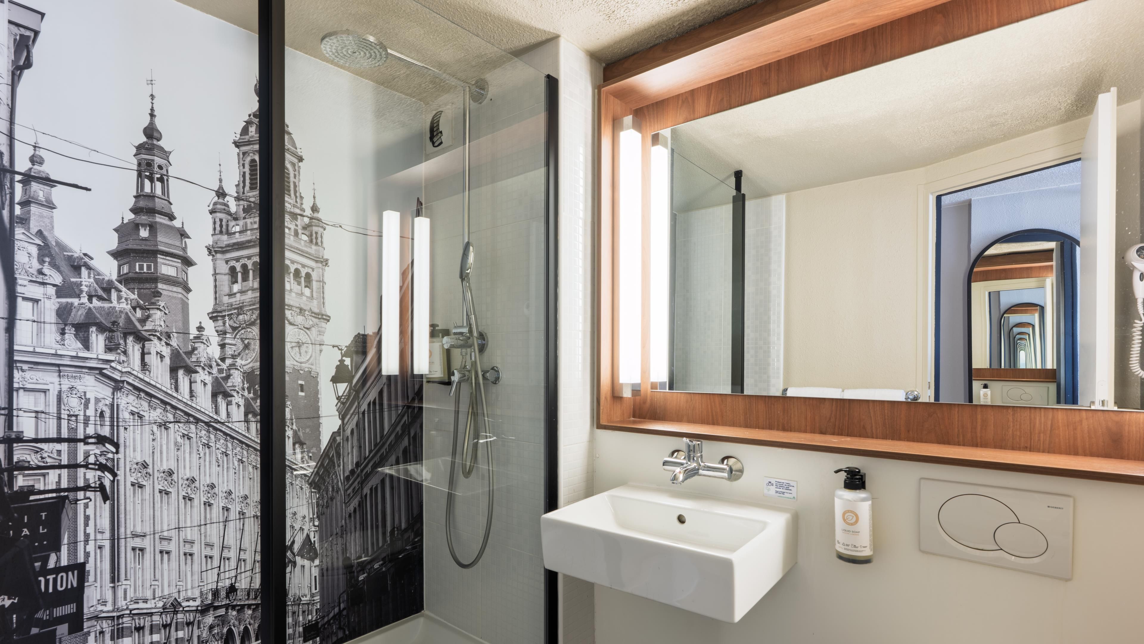 Un bagno con cabina doccia in vetro, un lavandino con specchio e un'immagine di un edificio storico.