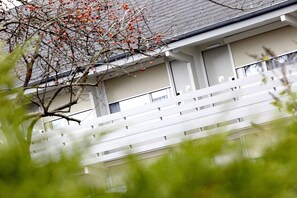 Ein Gebäude mit weißer Fassade, zahlreichen Fenstern und einem Baum mit roten Beeren im Vordergrund.