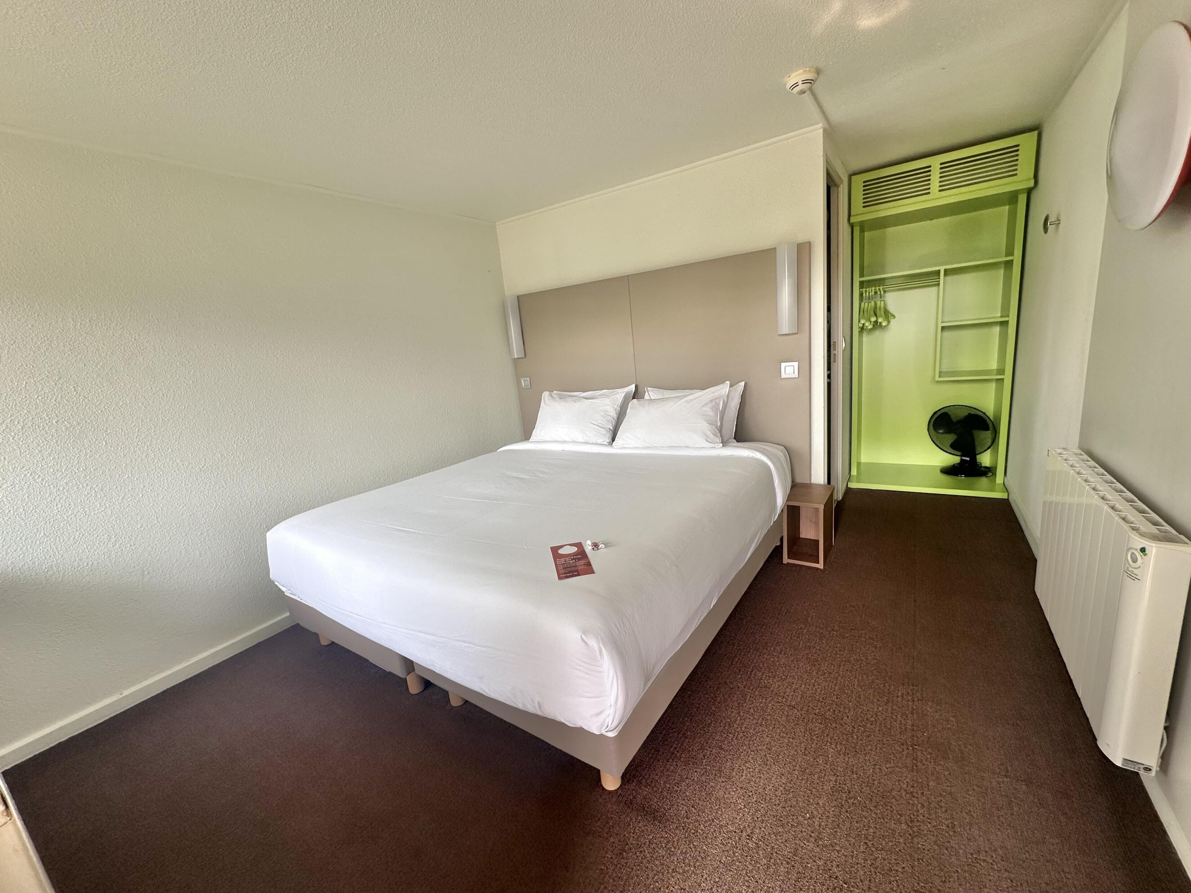 Une chambre d’hôtel avec un lit, une table de chevet, un radiateur et une porte verte donnant sur une salle de bain.