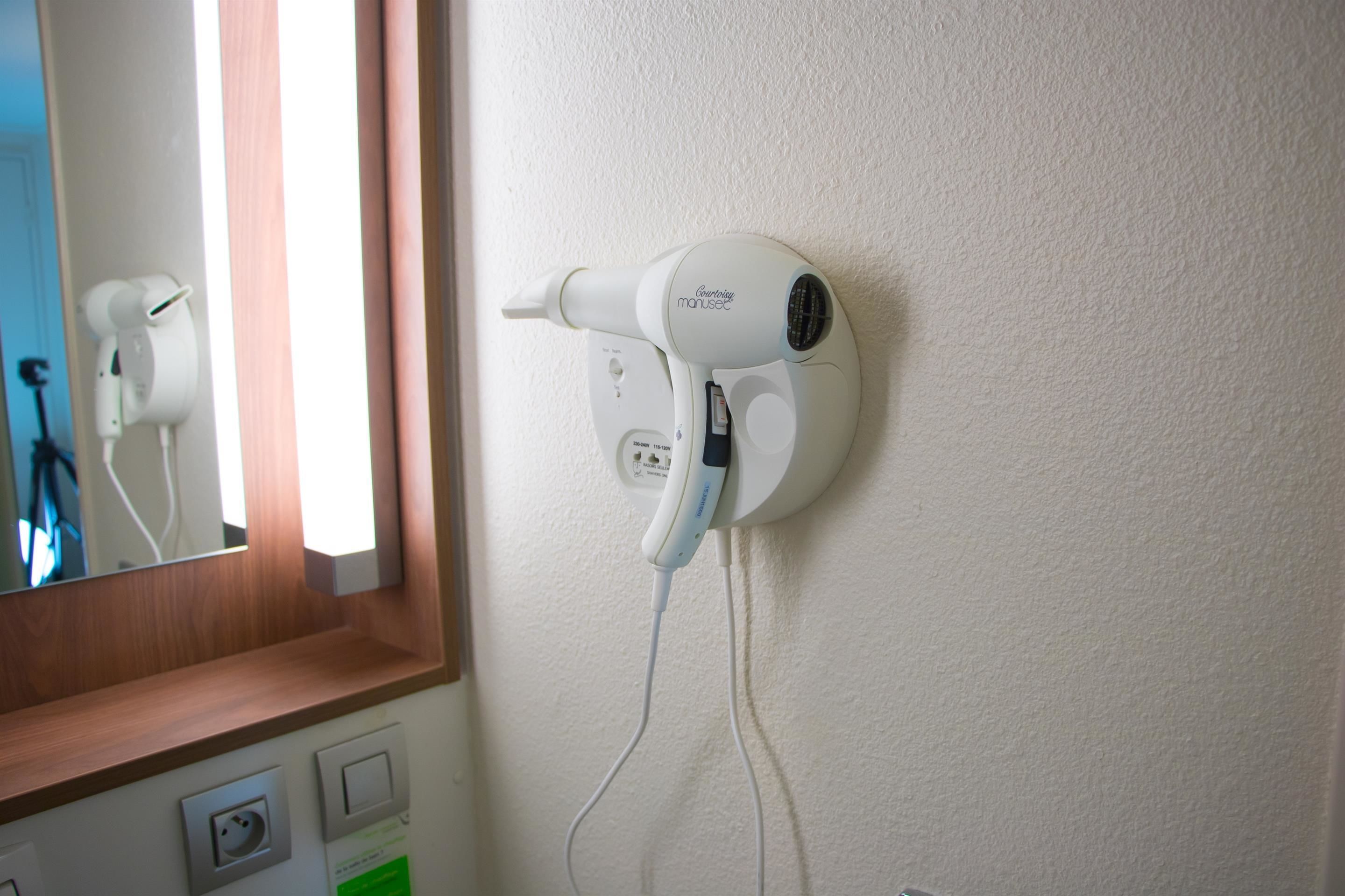 Un sèche-cheveux fixé au mur, avec un miroir au-dessus.