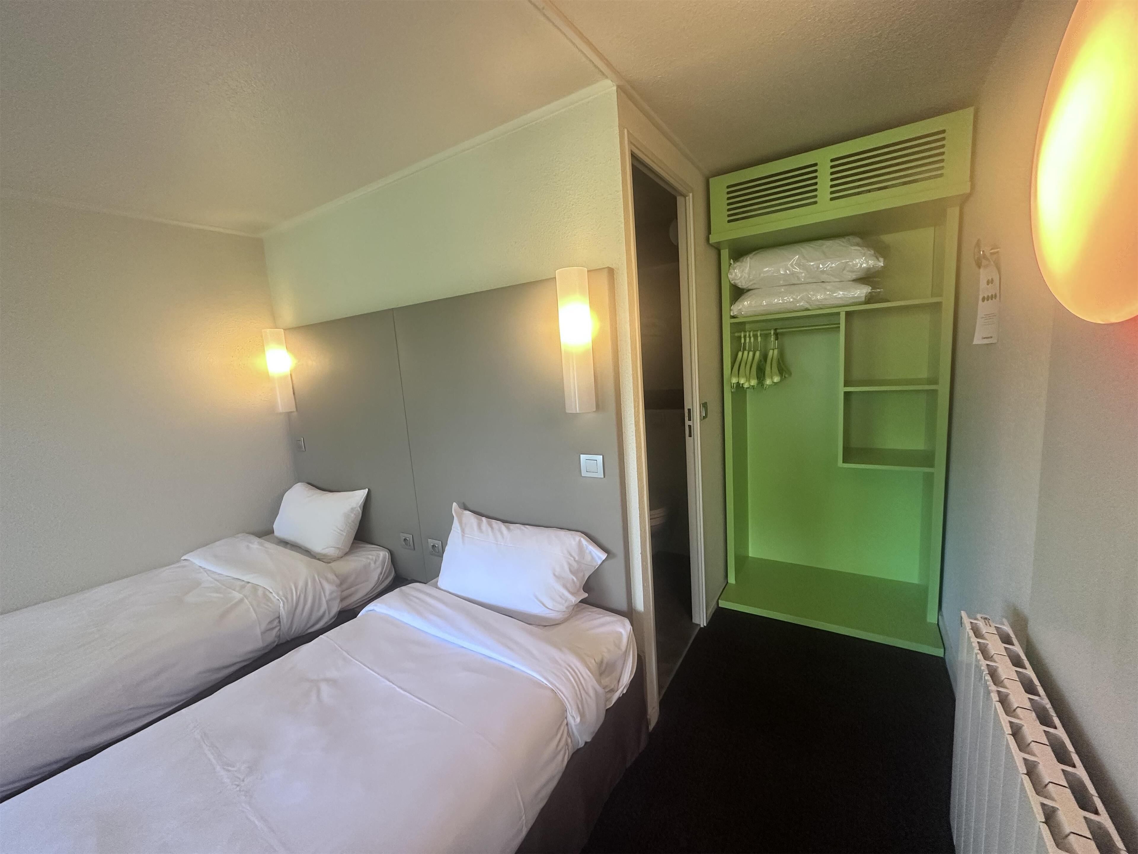 Habitación de hotel con dos camas individuales, un armario verde y un radiador.