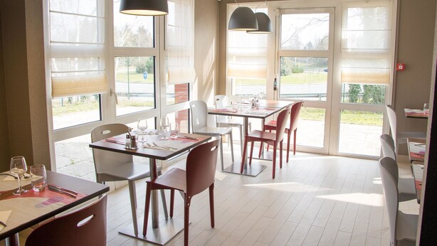 Un restaurant avec des tables et des chaises, de grandes fenêtres et des luminaires suspendus.