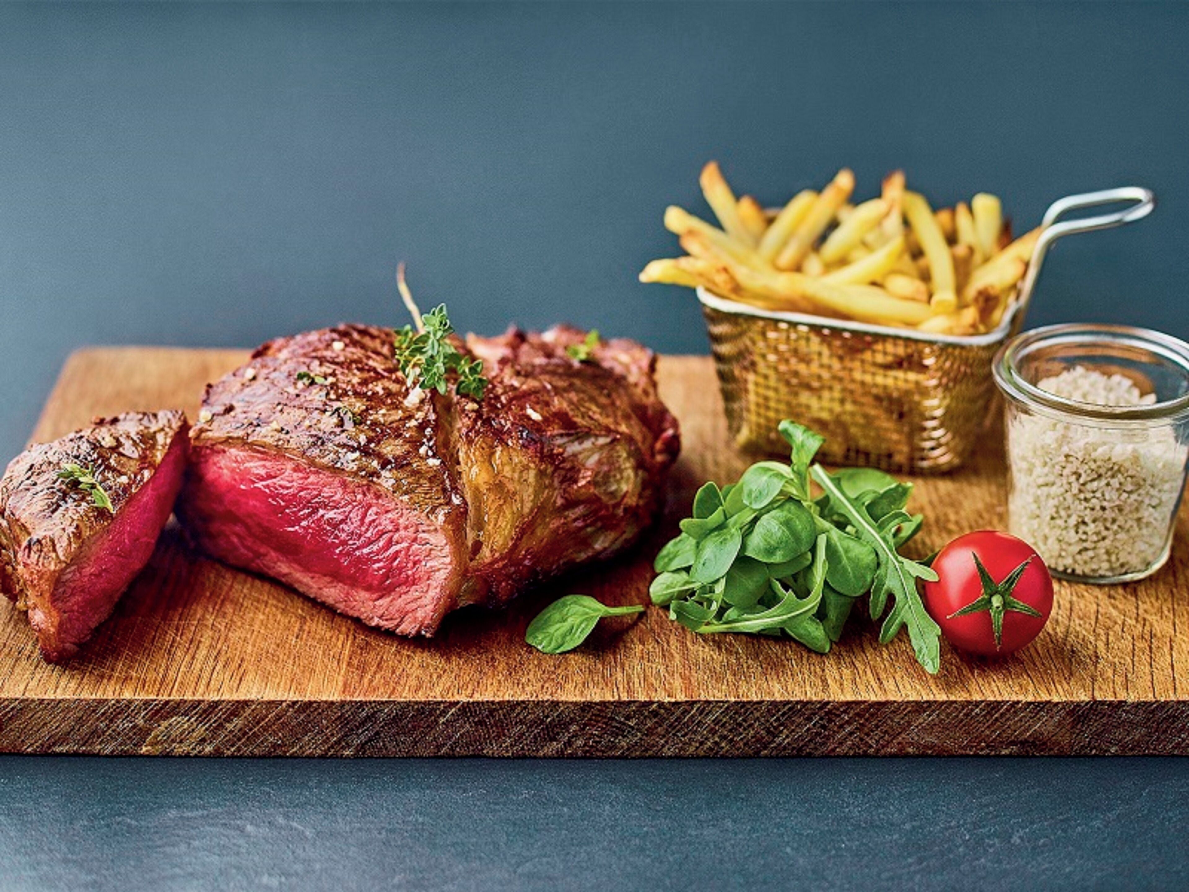 Un steak accompagné de frites et d’un petit bol d’assaisonnement, le tout présenté sur une planche en bois.